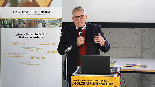 Es ist der Minister Backhaus am Rednerpult zu sehen. Linbks hinter ihm befindes sich ein Banner des Landesbeirates Holz.