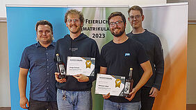 Lukas und Leif stehen gemeinsam mit zwei Ausgezeichneten, diese mit BLumen und Urkunden in der Hand, gemeinsam vor einer Bannerwand, auf der Feierliche Immatrikulation 2023 steht